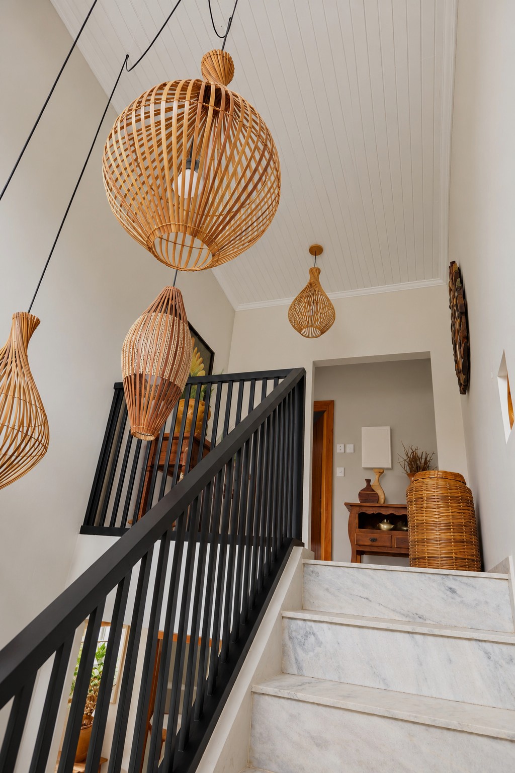 Elegant staircase in a modern boutique guesthouse, featuring natural stone steps, sleek black metal railings, and sculptural woven rattan pendant lights.