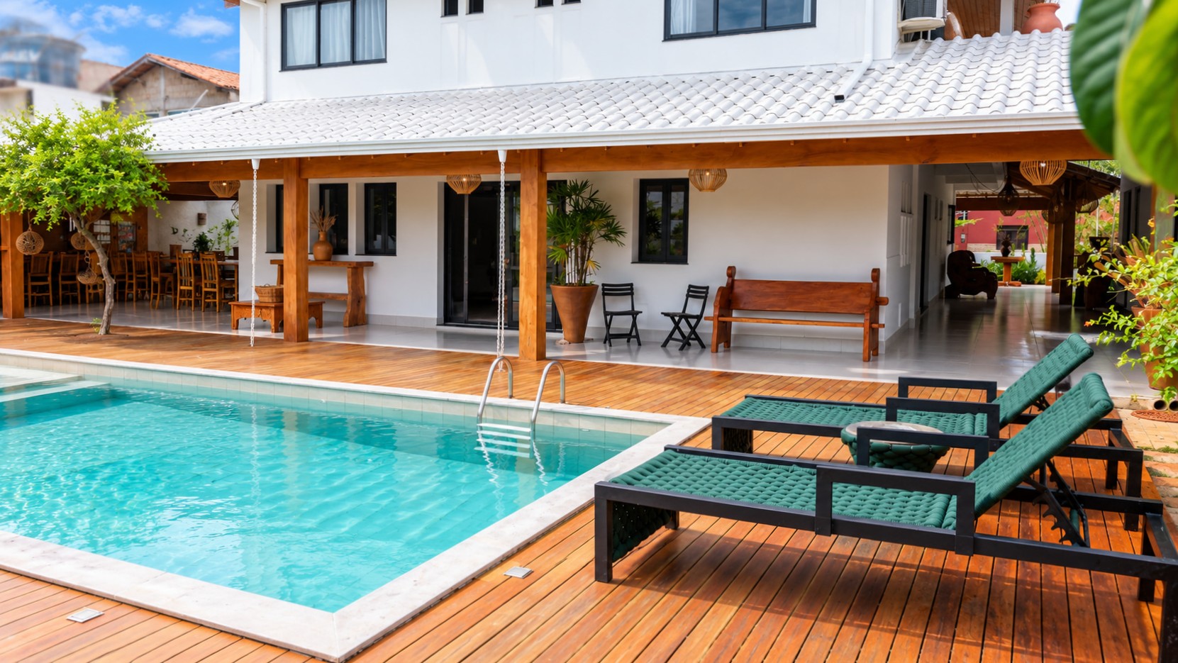 Spacious pool terrace at a boutique hospitality property, featuring cushioned lounge chairs, an expansive wood deck, and a covered communal veranda.