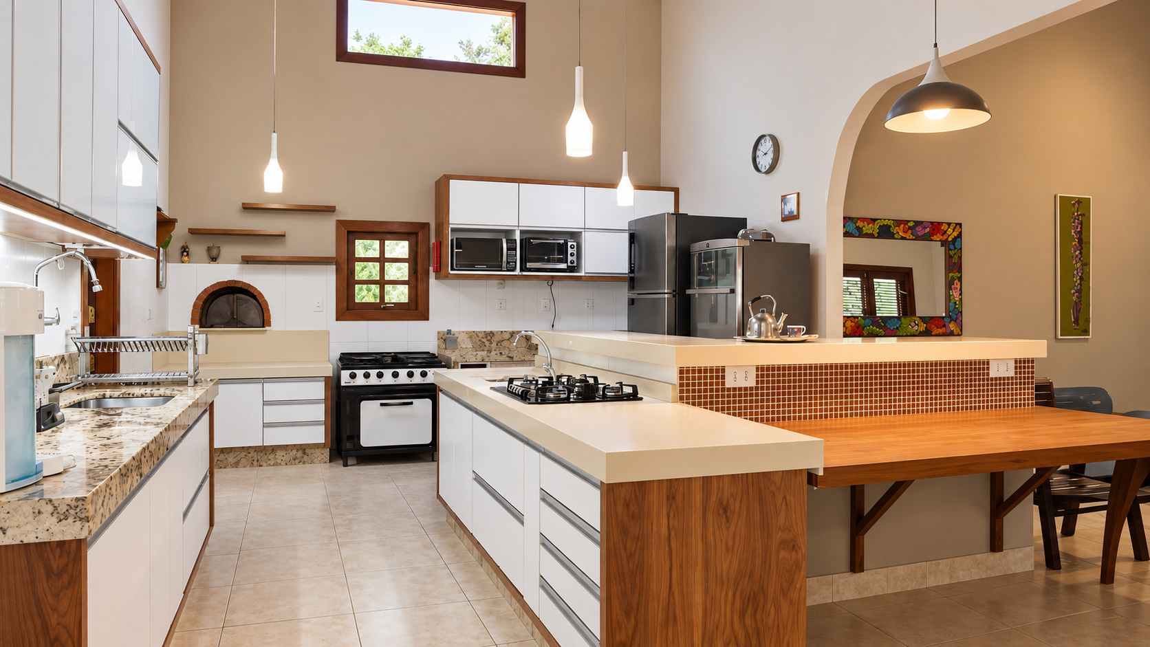 Helle, großzügige Küche der Strandimmobilie mit Kochinsel, Granitarbeitsplatten, gemauertem Pizzaofen und eleganter Frühstückstheke.