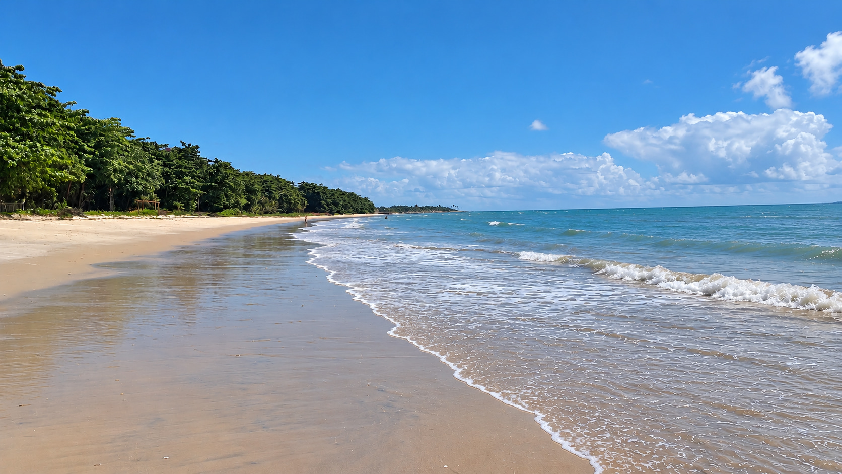Weitläufiger Sandstrand direkt vor dem zum Verkauf stehenden Ferienhaus in Bahia mit sanfter Atlantikbrandung und tropischer Küstenvegetation.