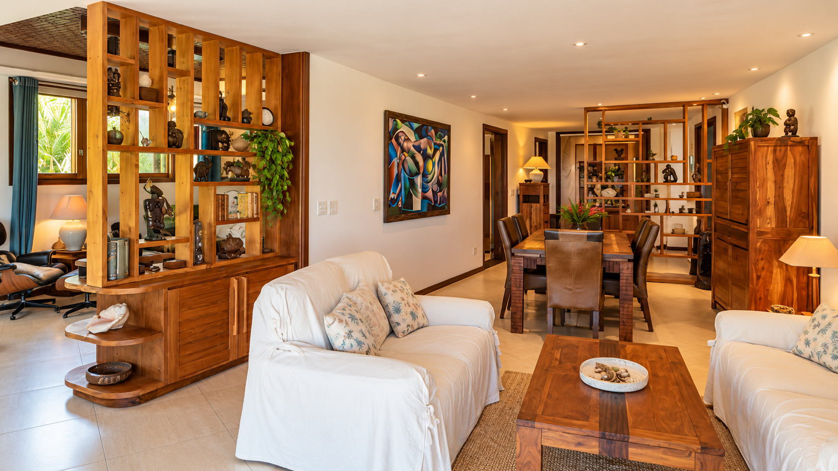 Großzügiger Wohn- und Essbereich einer exklusiven Küstenimmobilie in Brasilien mit hellen Sofas, offenen Holzregalen und eleganten Naturholzmöbeln.