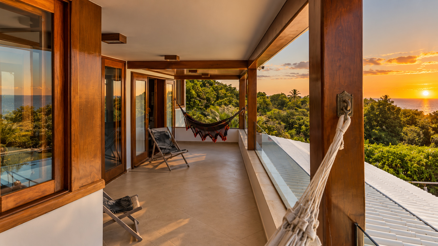 Überdachte Veranda im Obergeschoss einer exklusiven Strandvilla in Bahia mit Hängematten, Glasbrüstung und weitem Atlantikblick bei Sonnenuntergang.